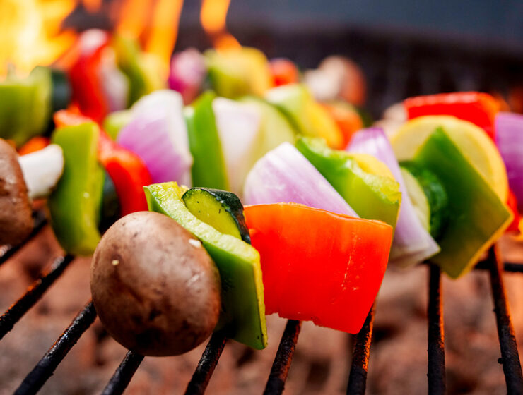 Close-up of colorful vegetable skewers with bell peppers, onions, zucchini, and mushrooms grilling over an open flame.