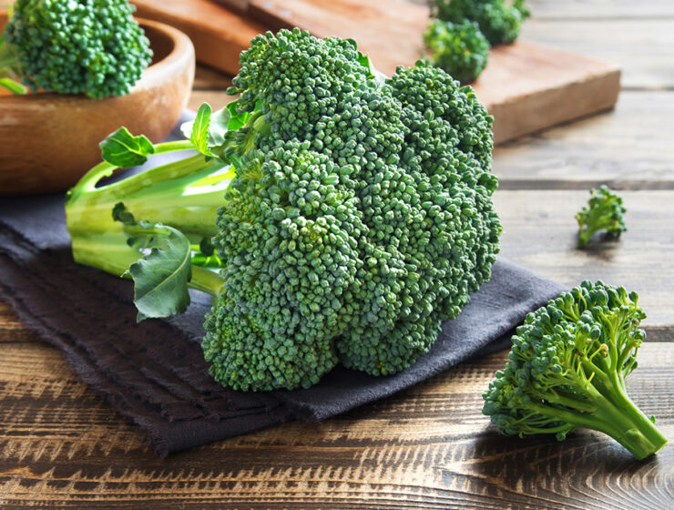 Fresh broccoli florets on a wooden table with a dark cloth, ready for cooking or serving.