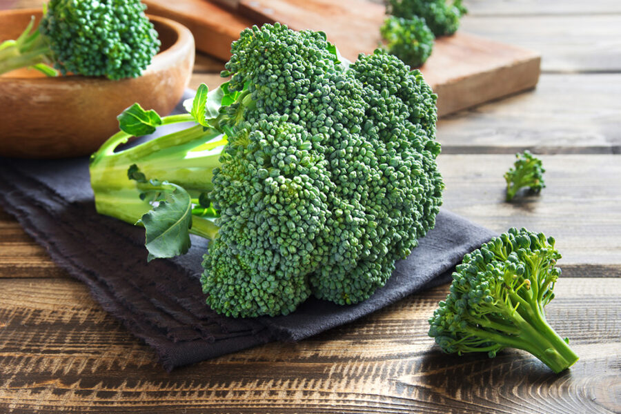 Fresh broccoli florets on a wooden table with a dark cloth, ready for cooking or serving.