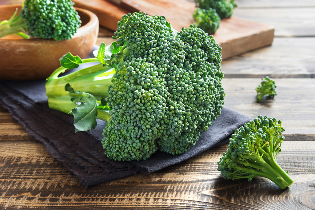 Fresh broccoli florets on a wooden table with a dark cloth, ready for cooking or serving.