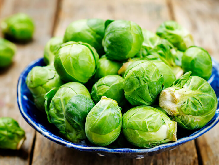 Fresh Brussels sprouts in a blue bowl on a wooden table, ready for cooking or serving.