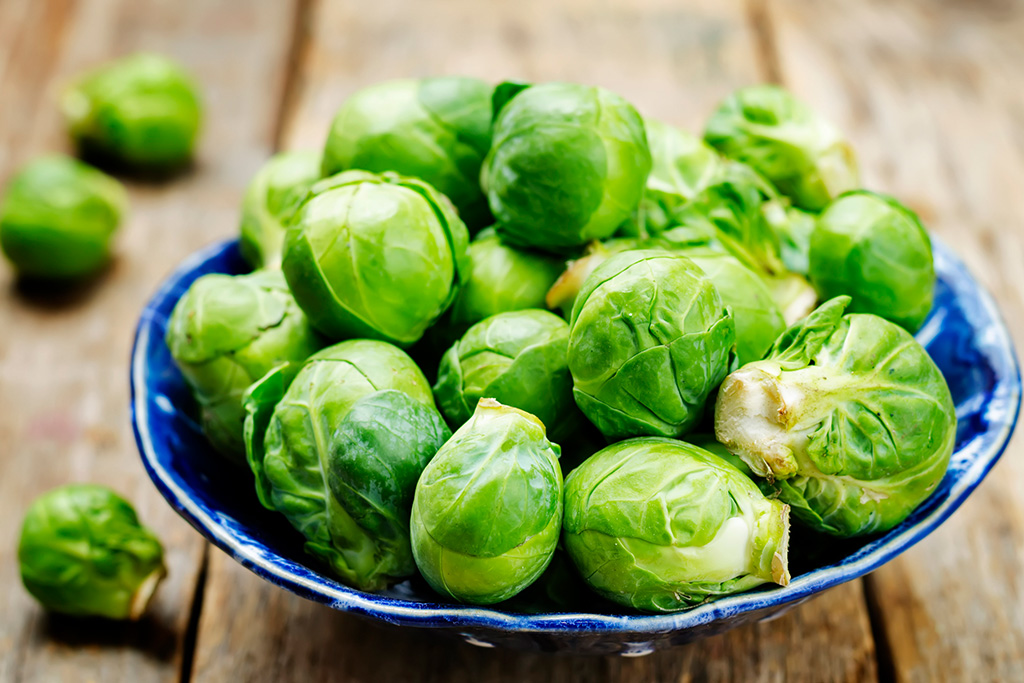Fresh Brussels sprouts in a blue bowl on a wooden table, ready for cooking or serving.
