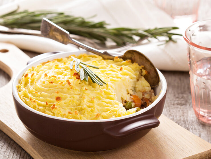 Shepherd's pie with golden mashed potato topping in a rustic dish, garnished with rosemary on a wooden board.