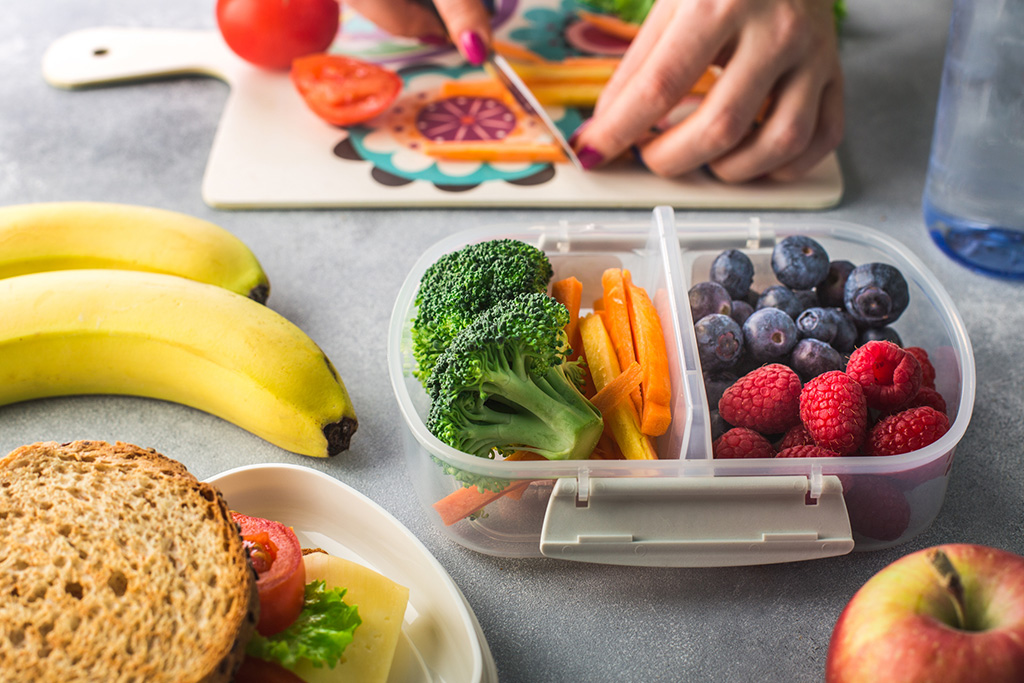 Healthy meal prep with fresh fruits and vegetables, including blueberries, raspberries, broccoli, carrots, bananas, and a sandwich, perfect for a balanced diet.