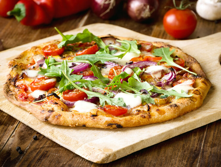 Freshly baked homemade pizza topped with arugula, tomatoes, red onions, and melted cheese on a wooden board.