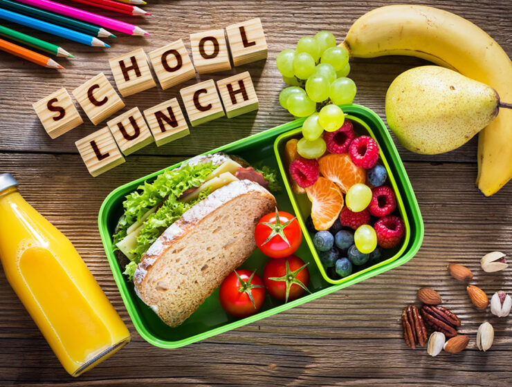 Healthy school lunch with sandwich, fruits, nuts, juice in green lunchbox, and 'School Lunch' in wooden blocks.