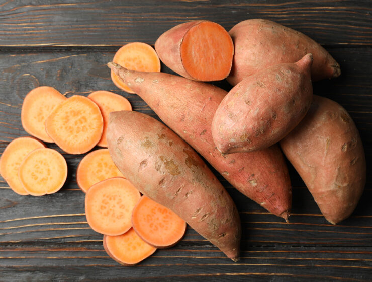 Raw sweet potatoes whole and sliced on dark wooden background.