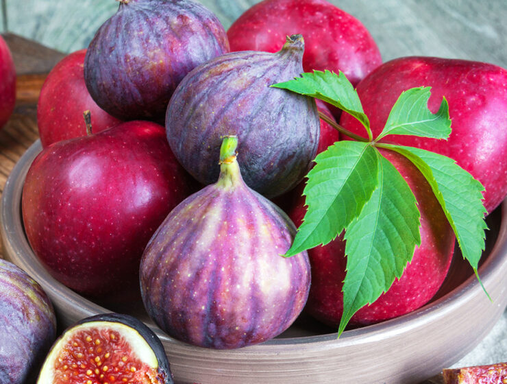 Fresh figs and red apples in a bowl with a green leaf garnish, creating a vibrant and healthy fruit display.