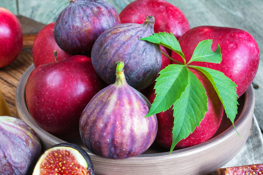 Fresh figs and red apples in a bowl with a green leaf garnish, creating a vibrant and healthy fruit display.