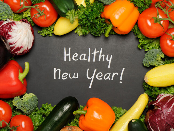 Chalkboard with 'Healthy New Year' surrounded by fresh vegetables like peppers, tomatoes, and zucchini.