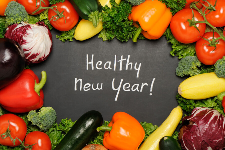 Chalkboard with 'Healthy New Year' surrounded by fresh vegetables like peppers, tomatoes, and zucchini.