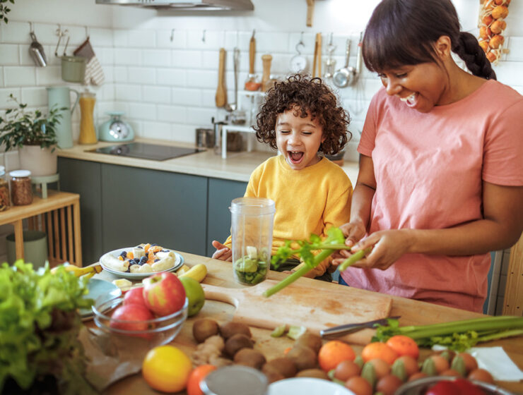 Mother and child preparing a healthy smoothie with fresh fruits and vegetables in the kitchen.