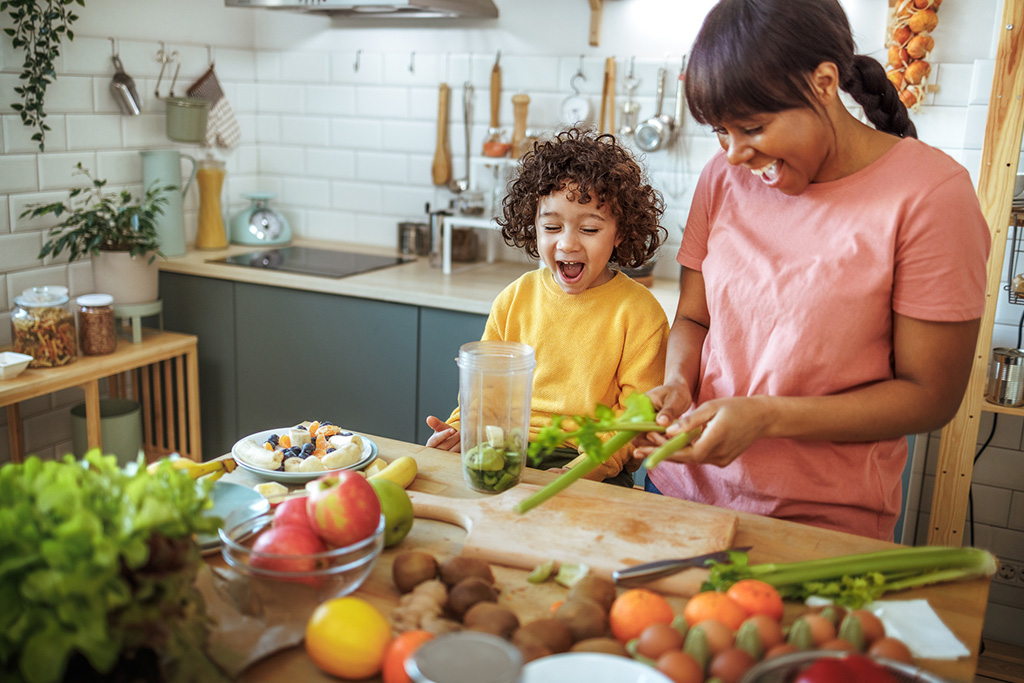 Mother and child preparing a healthy smoothie with fresh fruits and vegetables in the kitchen.