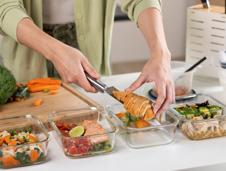 Person meal prepping healthy food with chicken, salmon, and vegetables in glass containers.